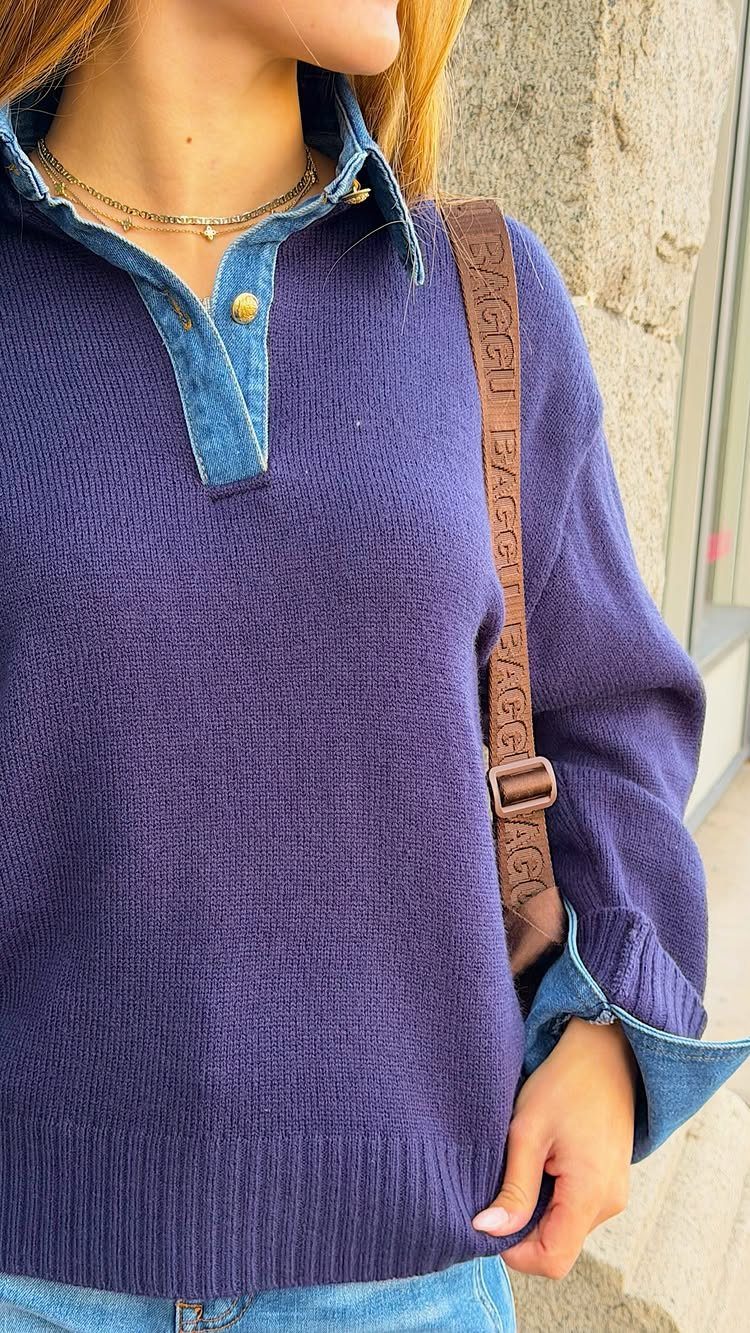 A person wearing a purple knit sweater with denim collar and cuffs and a brown bag.