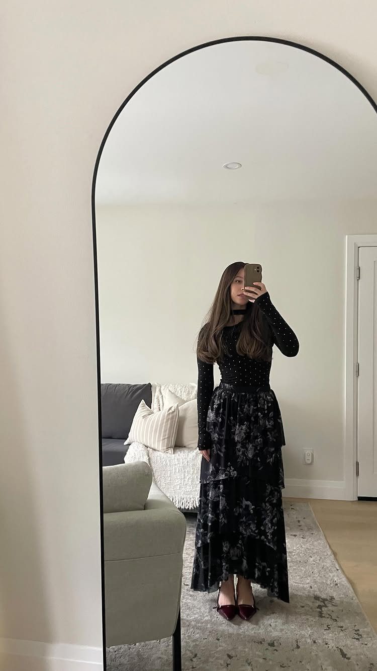 Woman in a black long-sleeved top and tiered black floral skirt posing in a mirror.