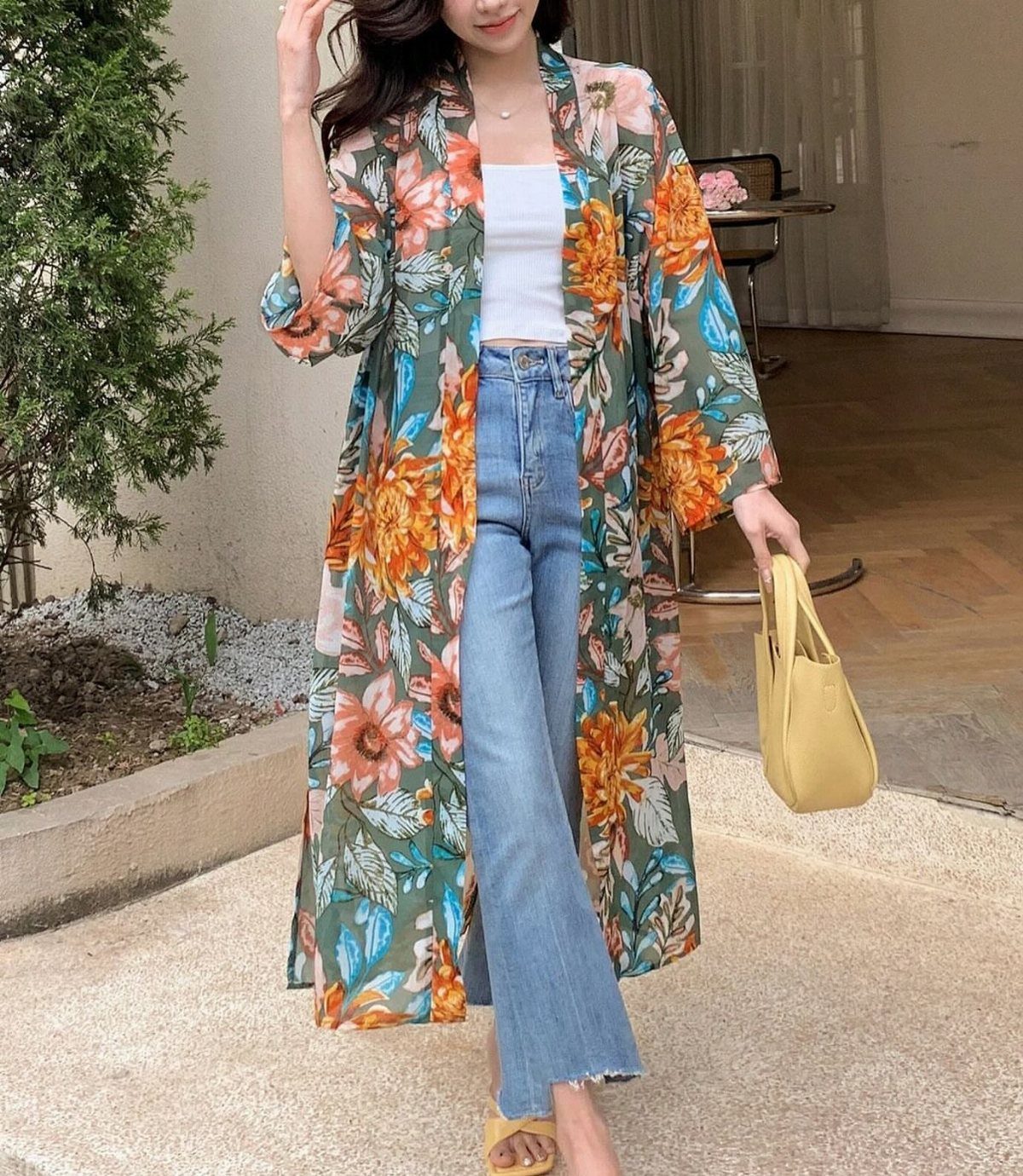 A woman wearing a long floral patterned kimono, white tank top, and blue flared jeans.