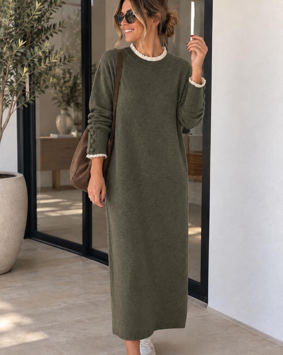 A woman posing in an olive green oversized knit sweater dress with white pearl trim.