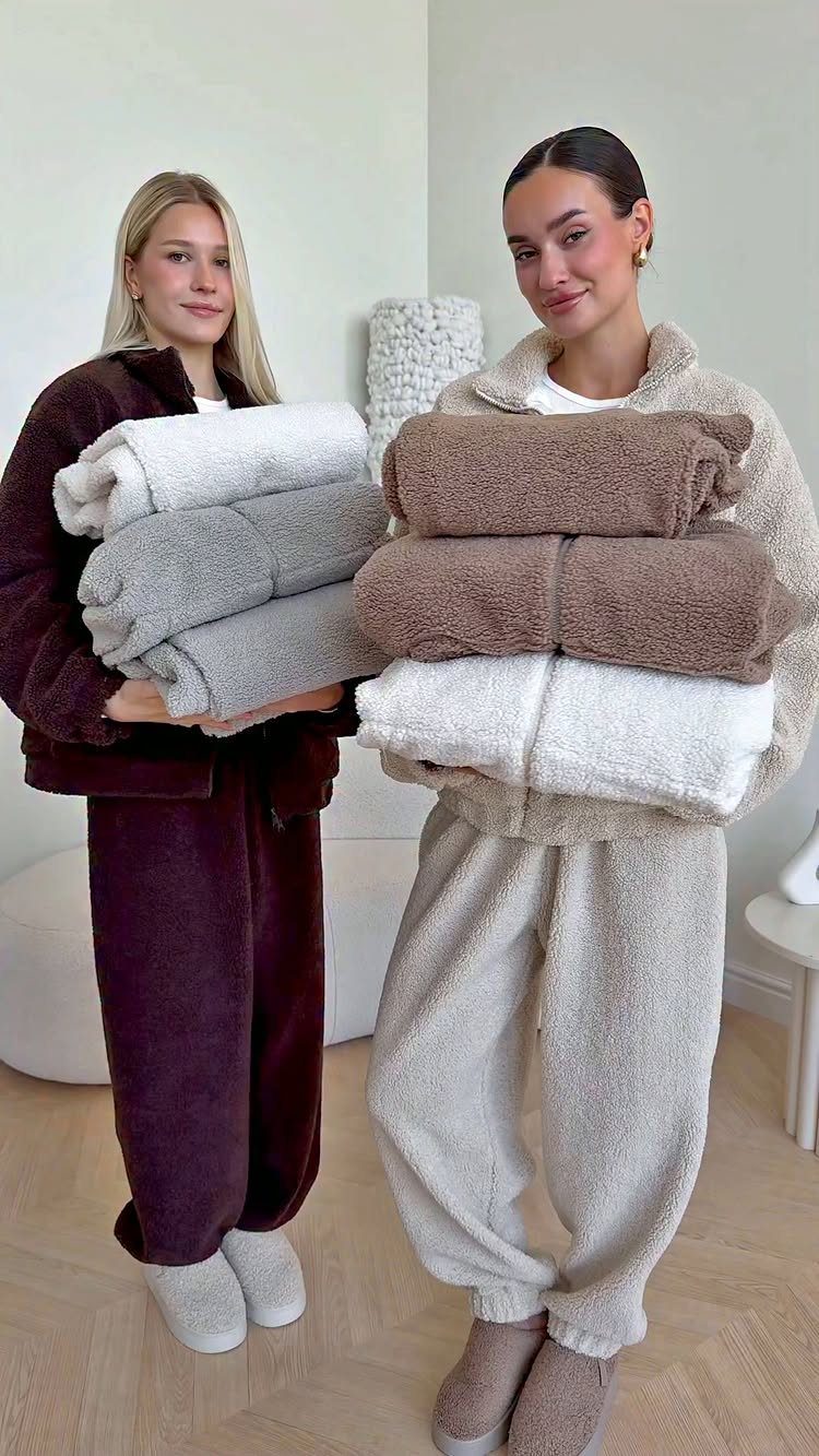 Two women in cozy fleece loungewear holding stacks of soft, folded blankets.