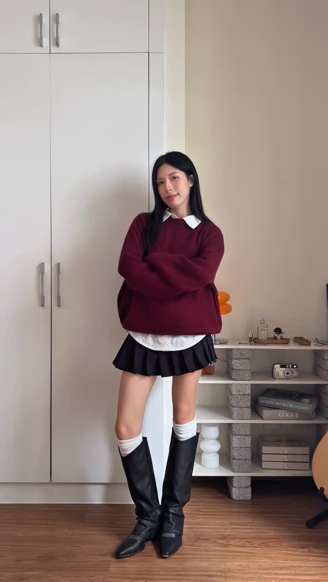Woman wearing a maroon sweater, white collared shirt, black pleated skirt, and black knee-high boots.