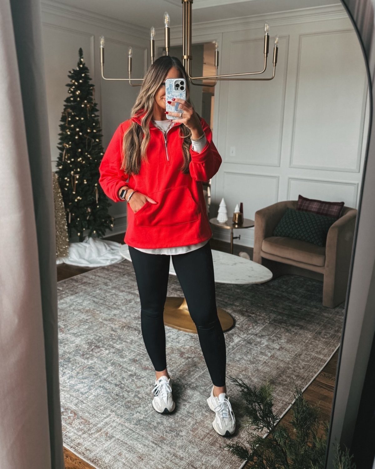 Woman in a red oversized sweatshirt and black leggings posing in a living room.