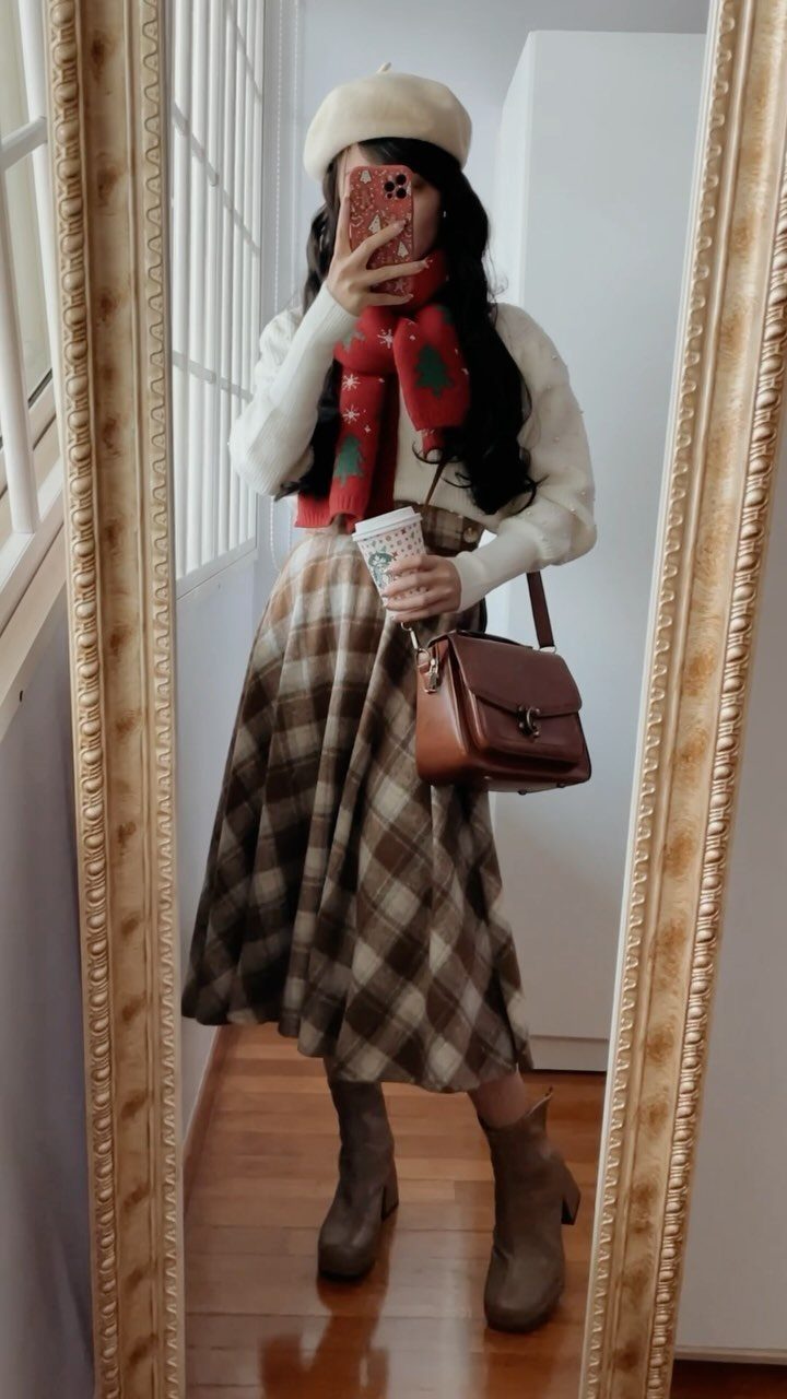 Woman in a white sweater, plaid skirt, and red scarf posing for a mirror selfie.