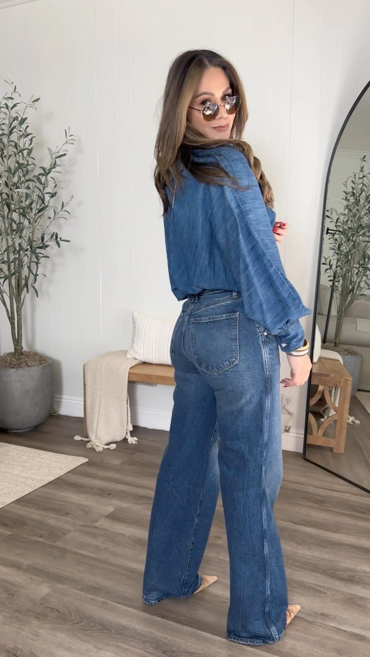 Woman posing in a blue denim shirt and wide-leg denim jeans indoors.