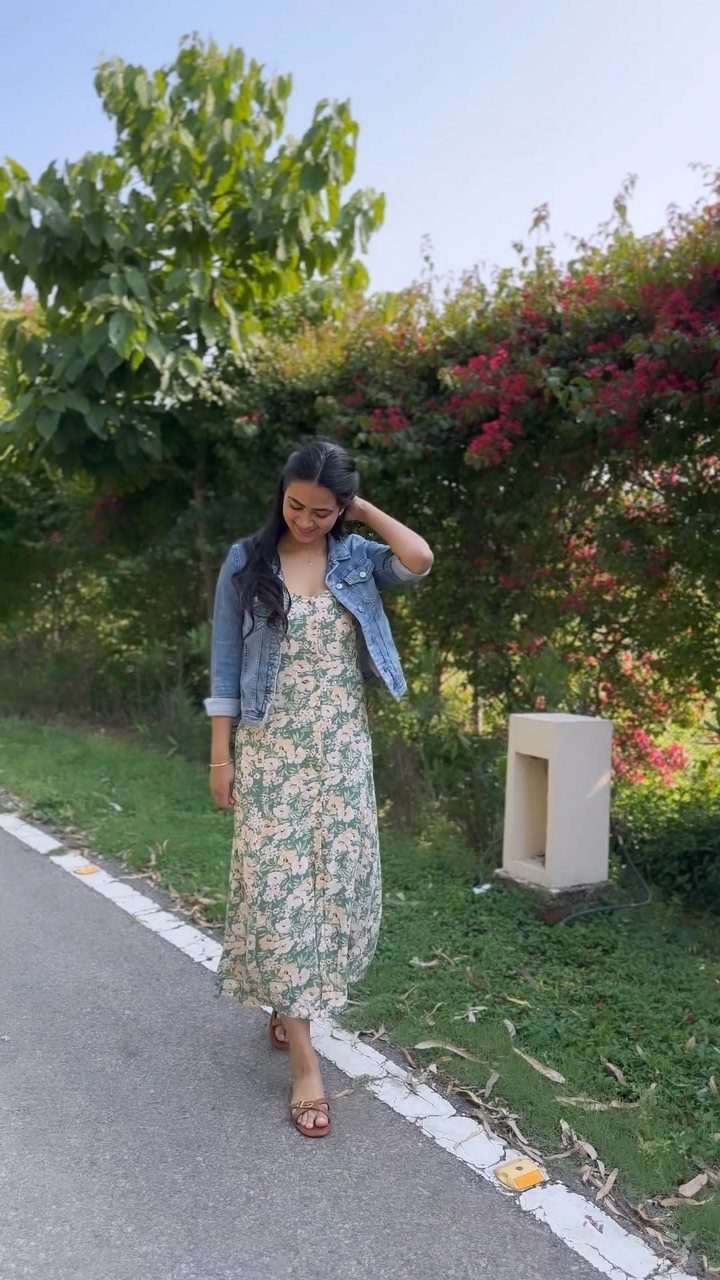 A woman wearing a floral maxi dress and denim jacket walking on a path.