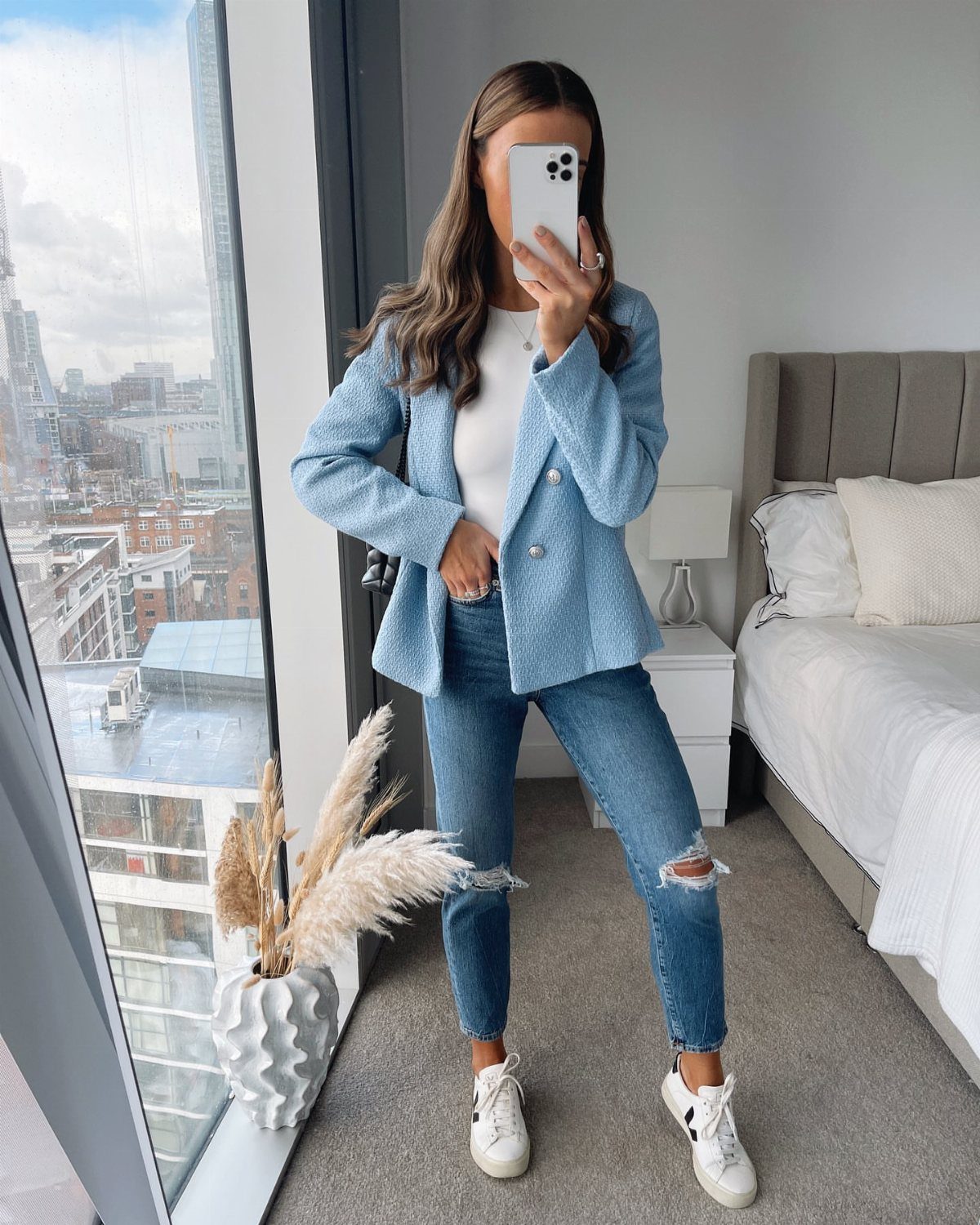 Woman in a blue blazer, white top, and ripped jeans posing for a mirror selfie.