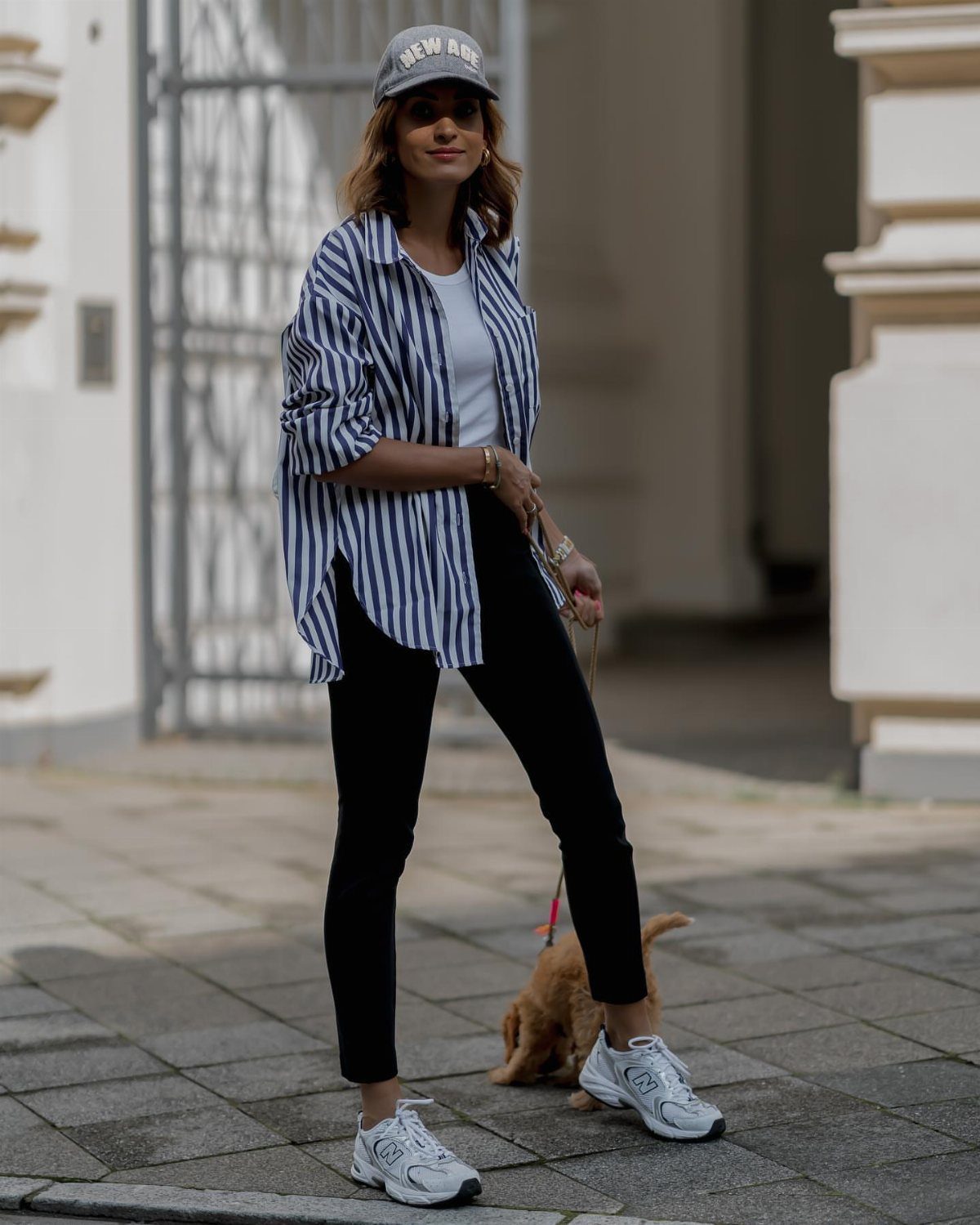 Woman wearing a striped shirt, white t-shirt, black leggings, and white sneakers outdoors.