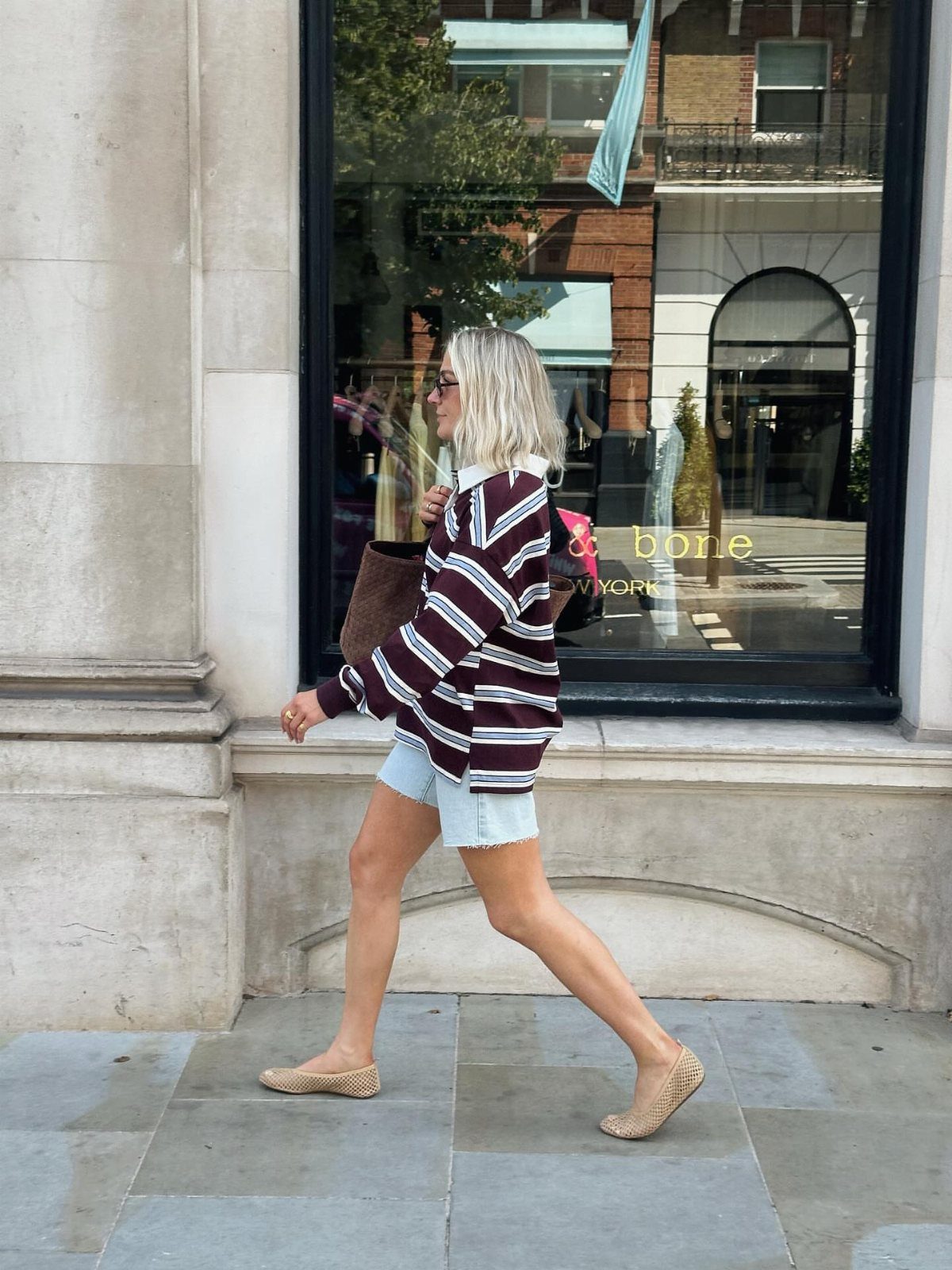 A blonde woman walking in a striped rugby shirt and denim shorts.