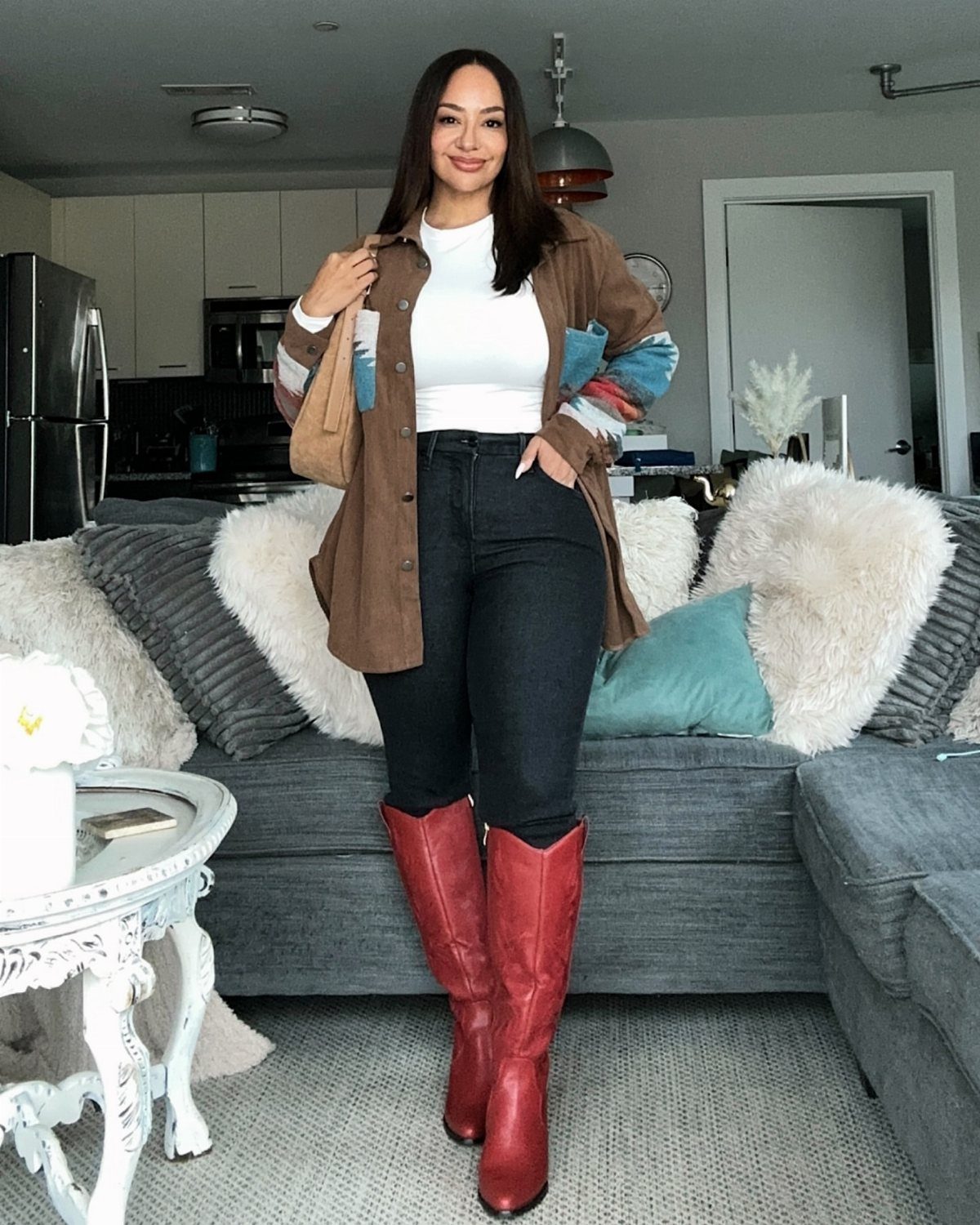 A woman wearing black jeans and tall red leather cowboy boots standing in a living room.