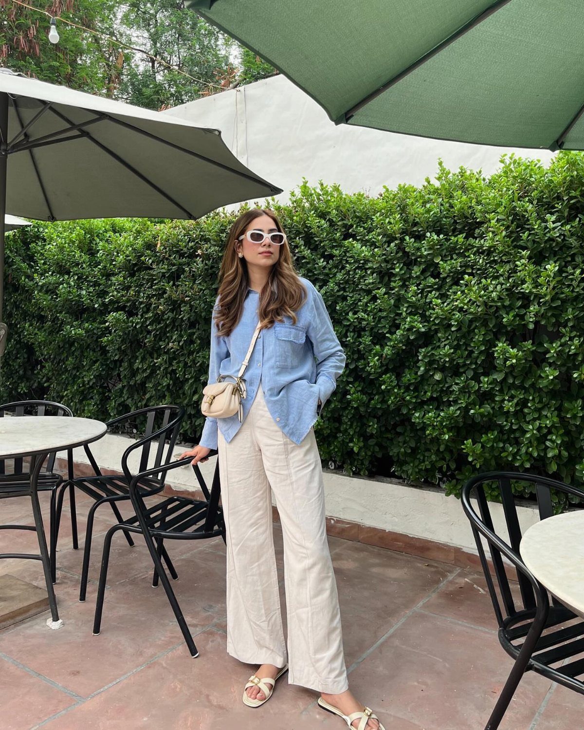 Woman wearing a light blue linen shirt and cream linen wide-leg pants standing outdoors.