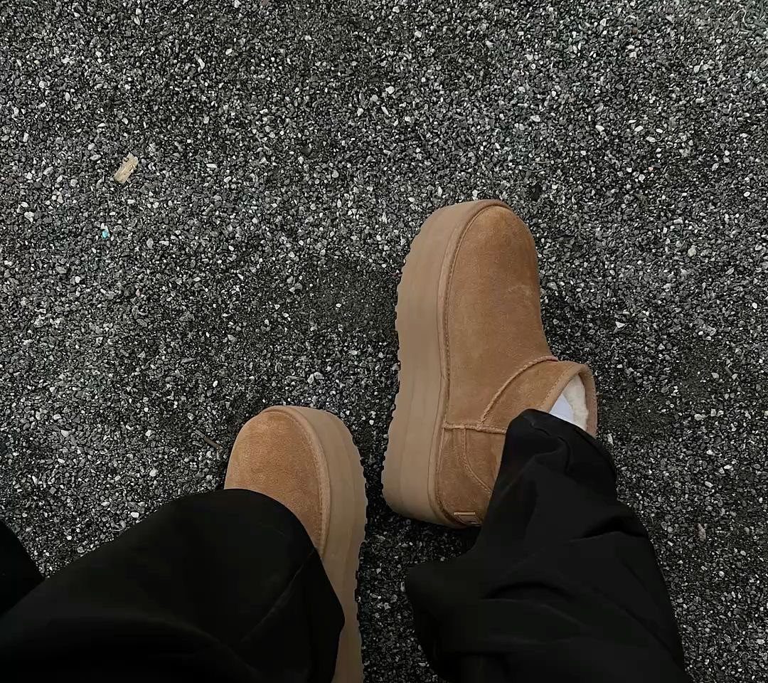 Tan suede platform boots worn with black trousers on an asphalt ground.