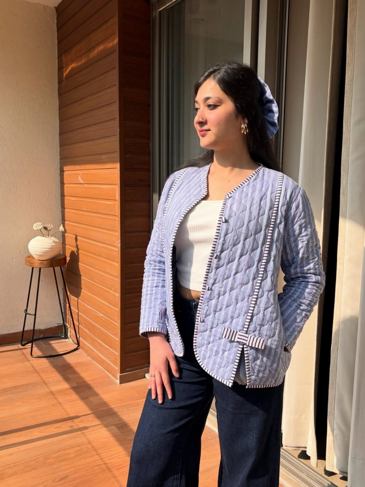 A woman wearing a light blue quilted jacket, white top, and dark denim jeans standing on a balcony.