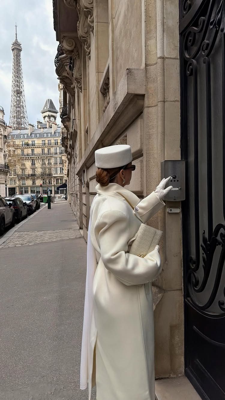 Woman in a cream winter coat and hat standing by a black door in Paris.