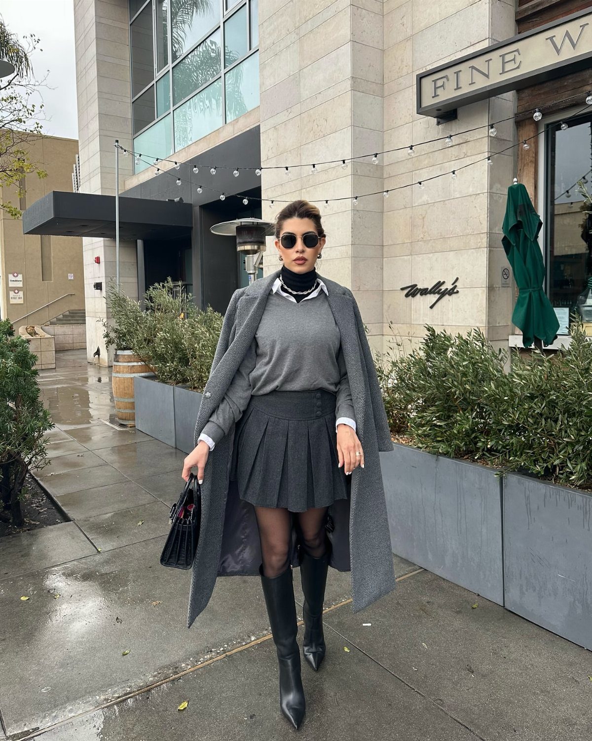 A woman posing in a chic grey winter outfit with a long coat and black boots.