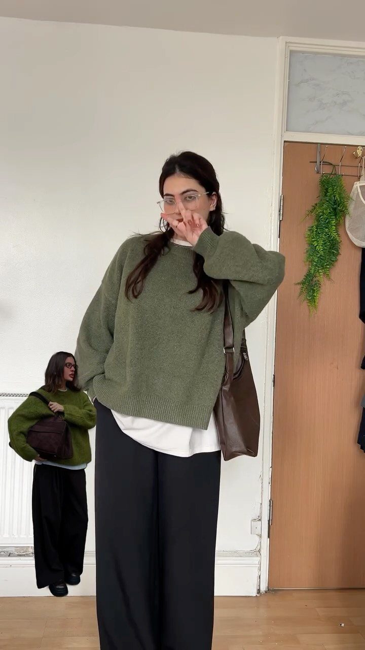 Woman wearing an olive green knit sweater, white undershirt, and black wide-leg trousers.
