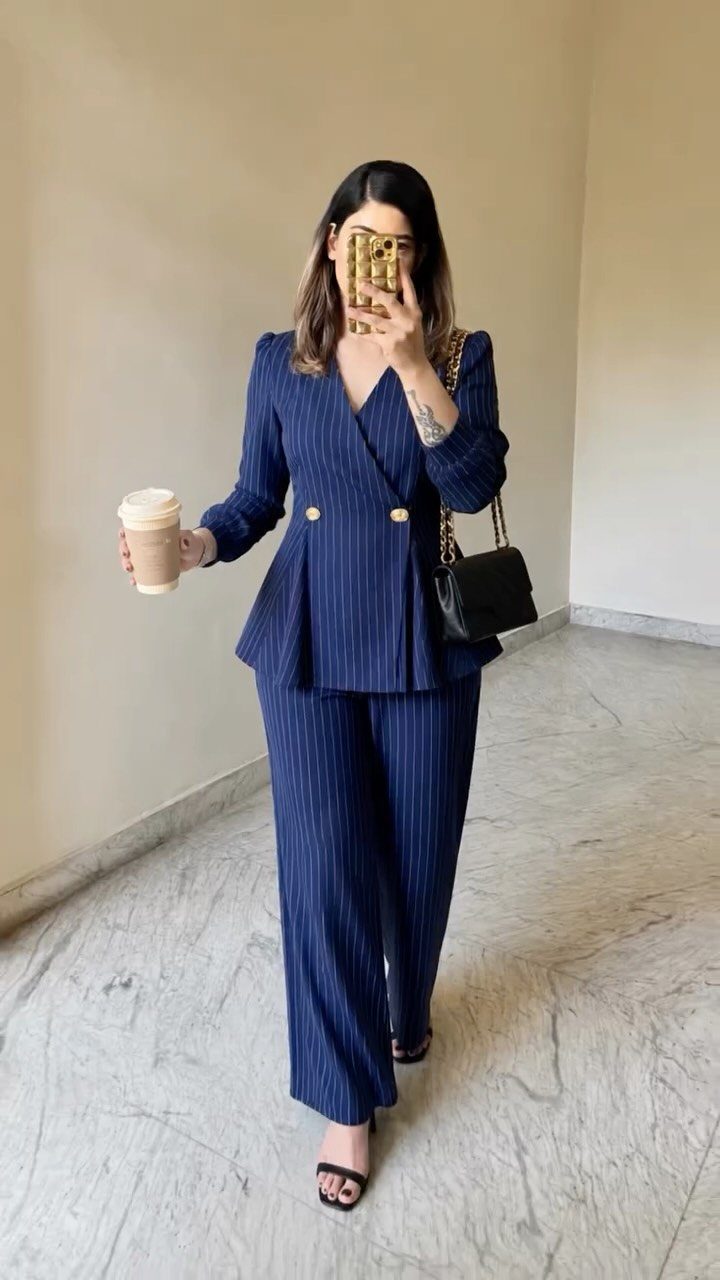 Woman in navy pinstripe blazer and matching wide-leg tailored trousers holding coffee.