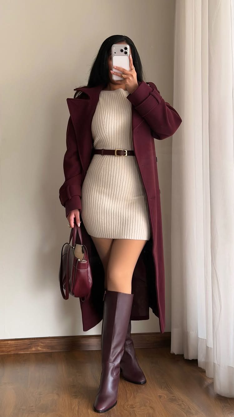 Woman wearing a beige sweater dress, burgundy trench coat, and burgundy knee-high boots.