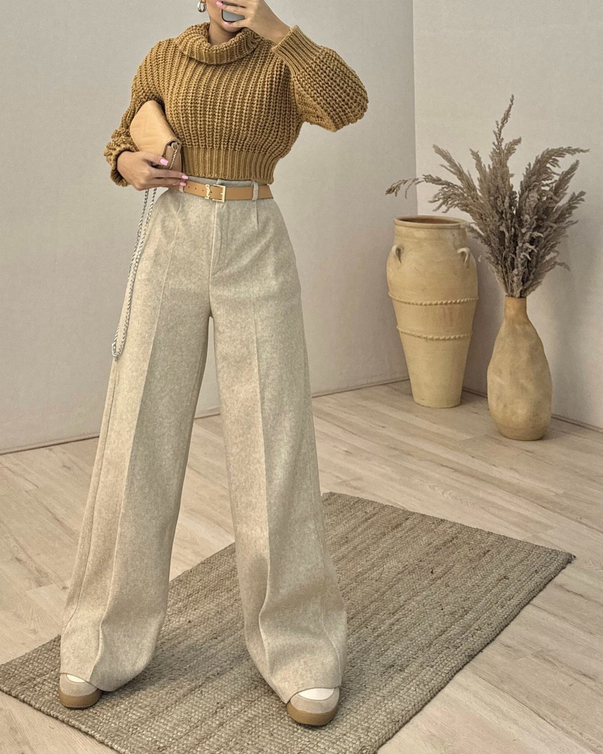 Person wearing a chunky brown knit sweater and beige wide-leg trousers standing in a neutral room.