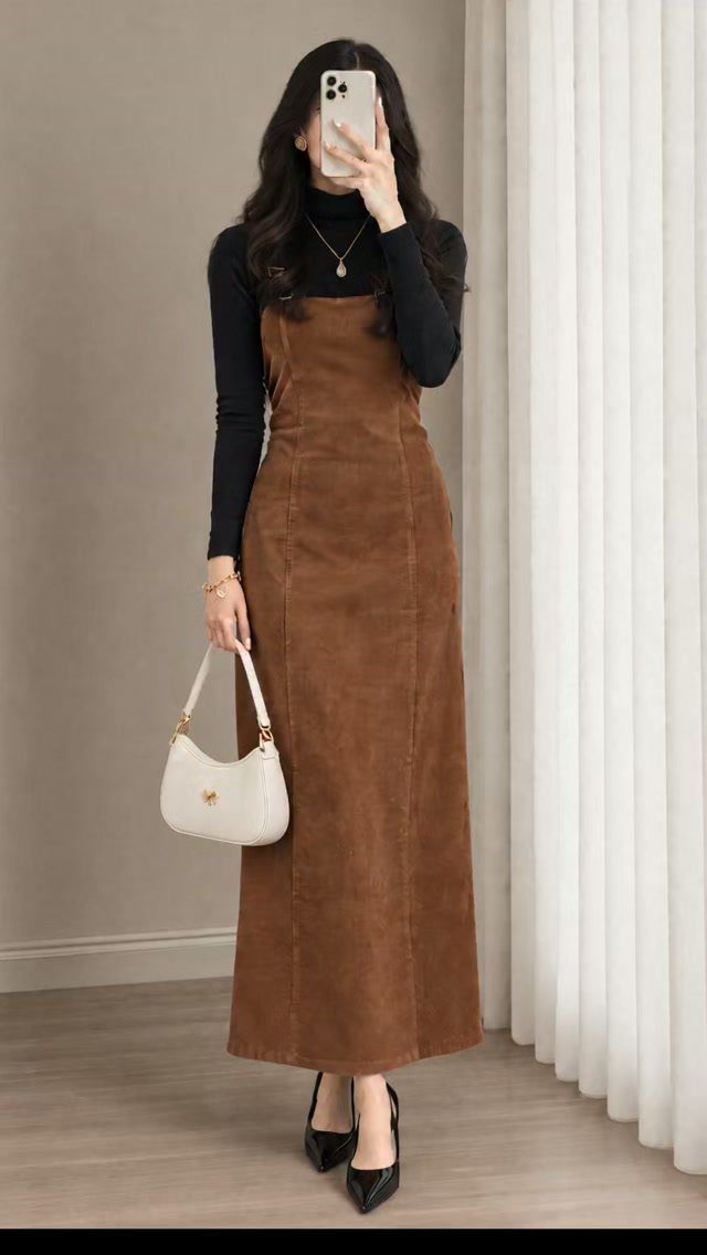 Woman in black turtleneck and brown corduroy maxi dress holding a white purse.