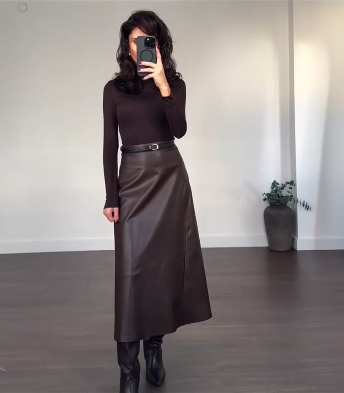 Woman in a dark brown turtleneck and faux leather maxi skirt posing for a mirror selfie.