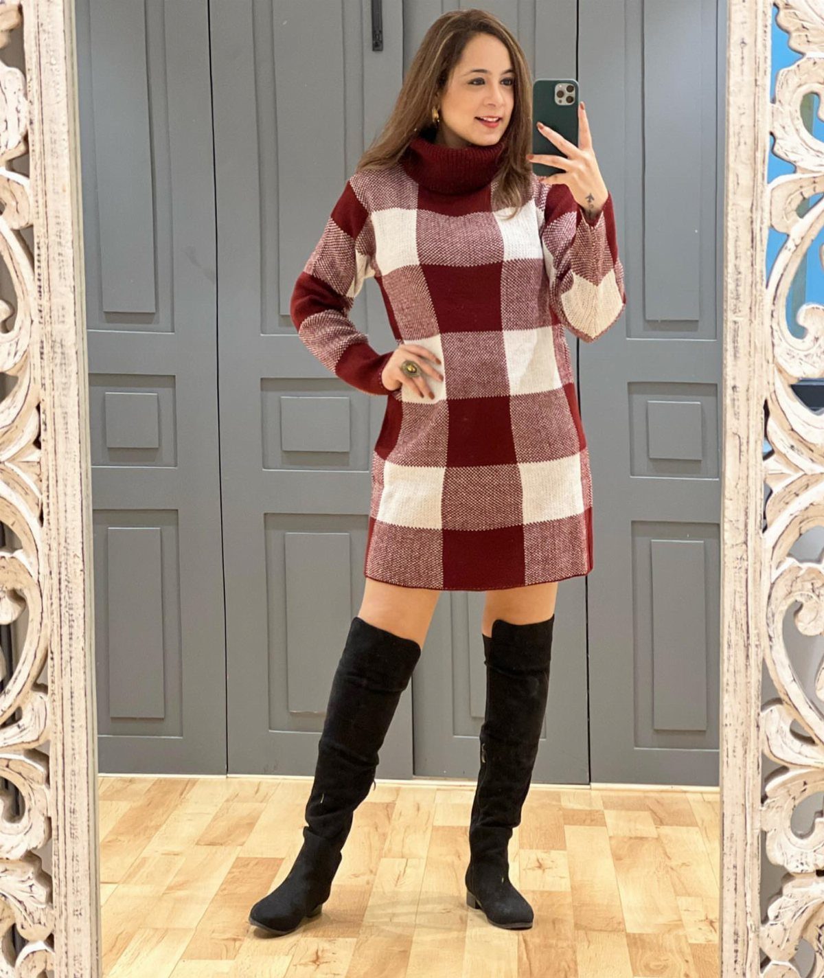 Woman in a checkered sweater dress and black over-the-knee boots posing for a selfie.