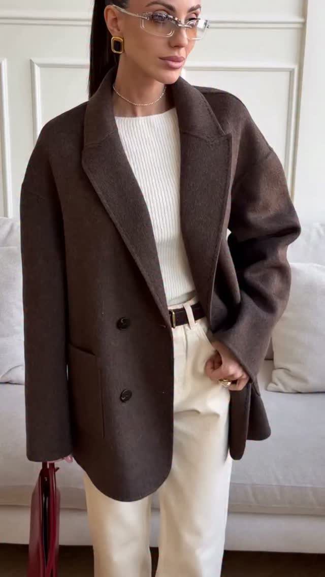 Woman wearing an oversized dark brown wool blazer over a white sweater and cream trousers.