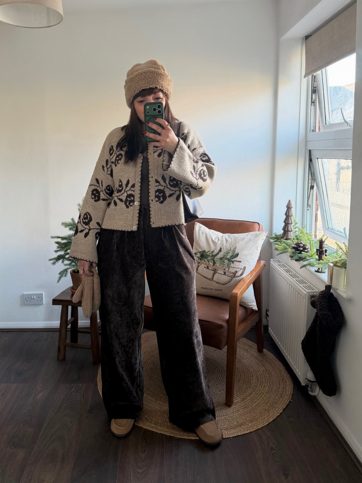 A person posing in a patterned chunky cardigan and dark corduroy trousers.