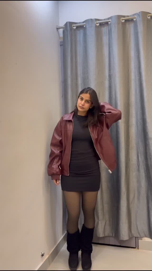 A woman posing in a maroon leather jacket, black dress, and black tights.