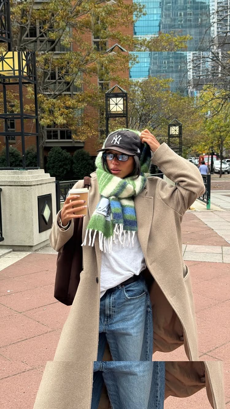 A person dressed in a beige coat and striped scarf standing on a city street.