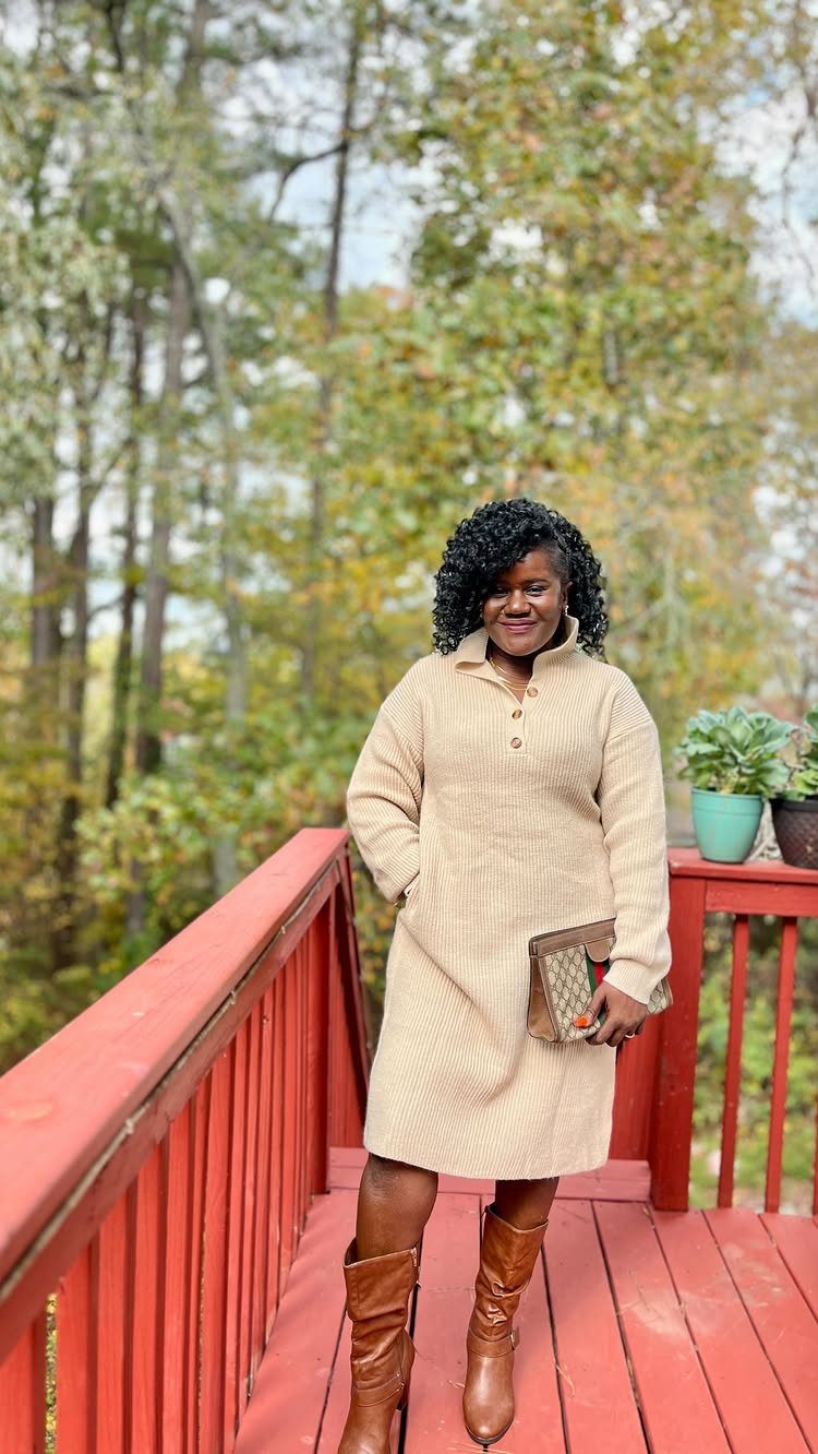 A woman wearing a beige button-up sweater dress and brown boots standing on a red deck.