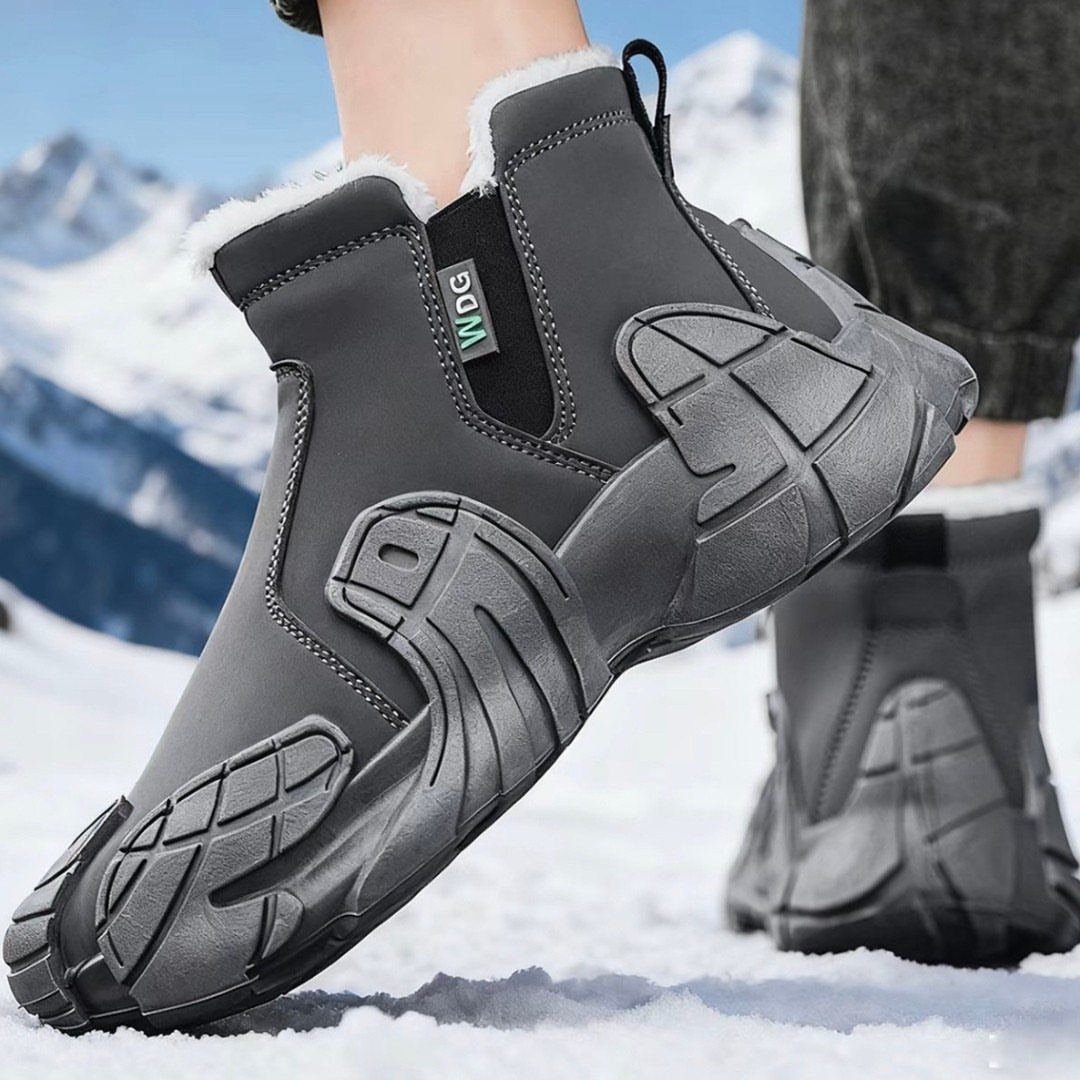 Black fleece-lined winter boots worn by a person standing in a snowy mountain landscape.