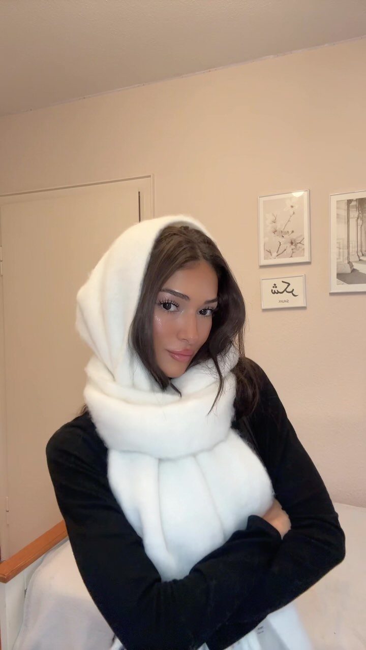 A woman wearing a large, white, fluffy hooded scarf over a black shirt.