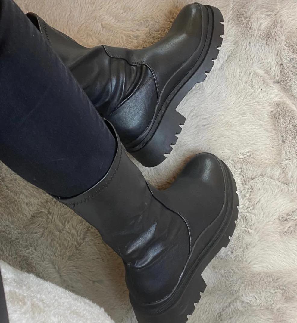 Black leather ankle boots with chunky lugged soles worn with dark trousers on faux fur.