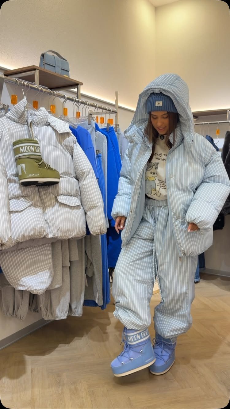 A person wearing a striped puffer jacket, matching pants, and blue boots in a clothing store.
