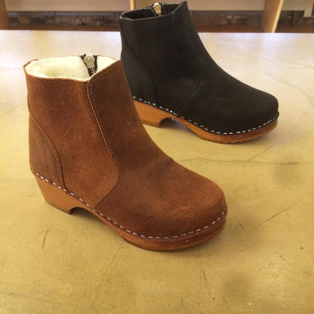 Two suede ankle boots with wooden soles, one brown and one black, on a tan surface.