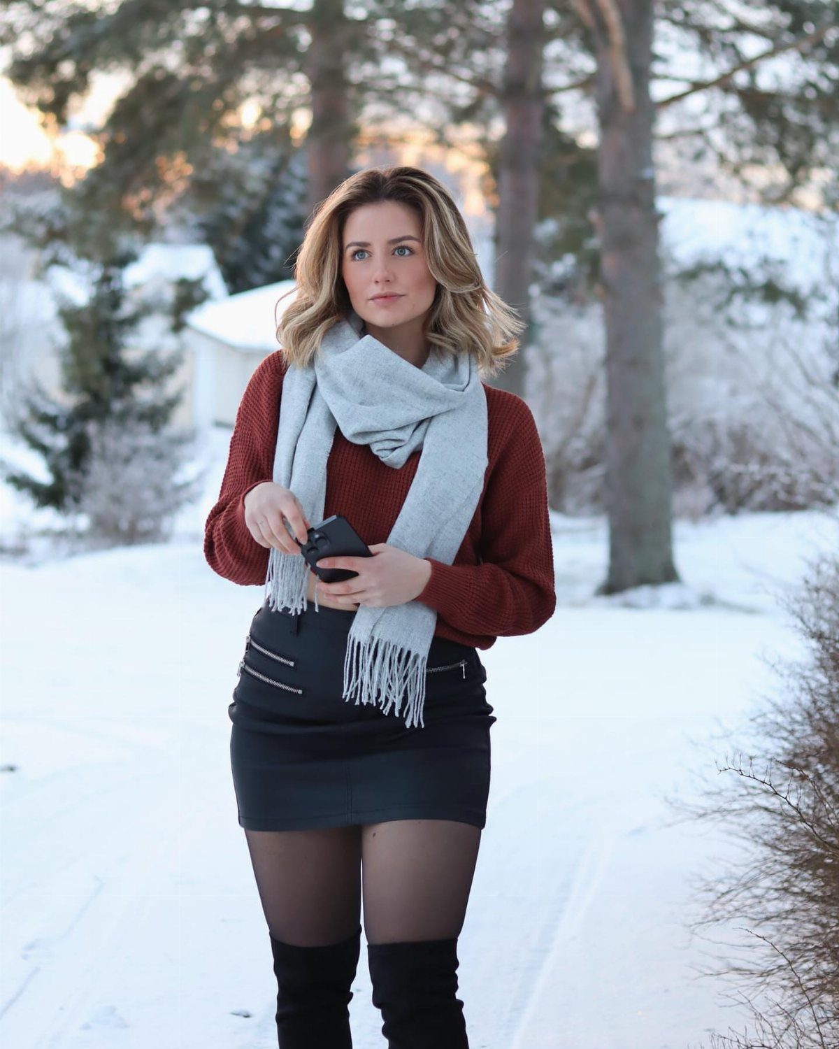 Woman in a rust sweater and black leather skirt standing in a snowy landscape.