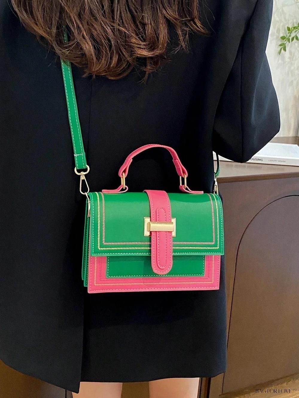 A green and pink handbag with a gold clasp hanging from a person wearing a black coat.