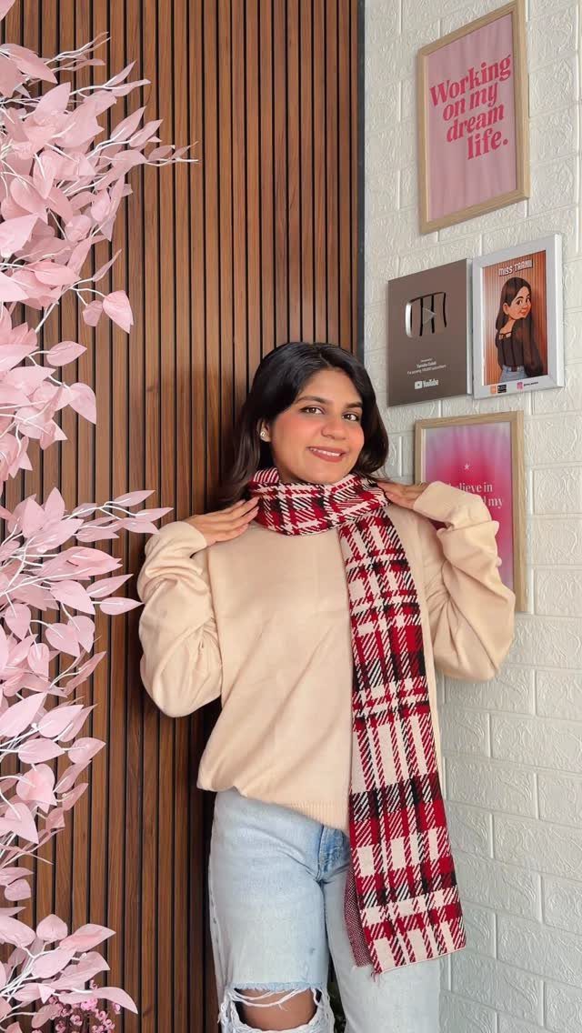 A woman wearing a cream sweatshirt and a red plaid scarf while smiling at the camera.