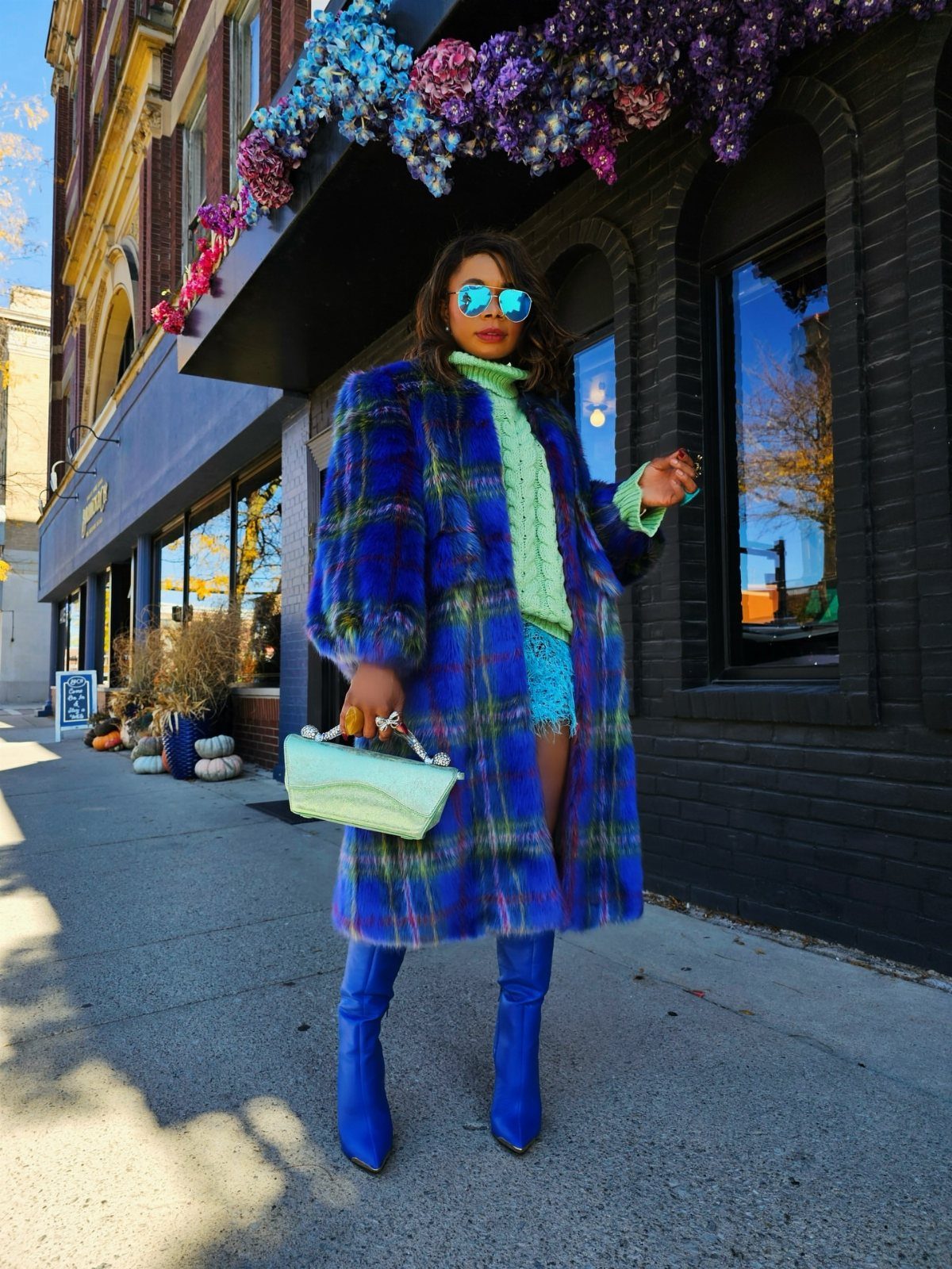 A woman posing in a blue and purple plaid faux fur coat and blue boots.