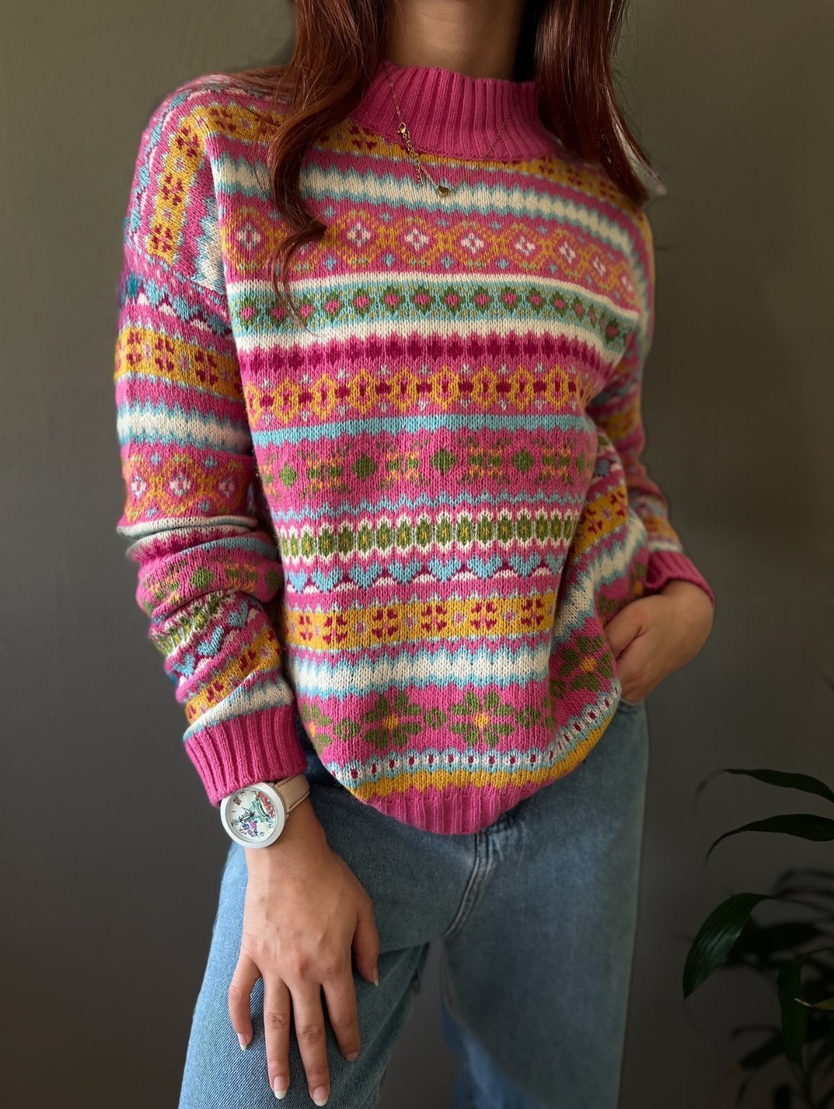 A person wearing a vibrant, multi-colored patterned knit sweater and light blue denim jeans.