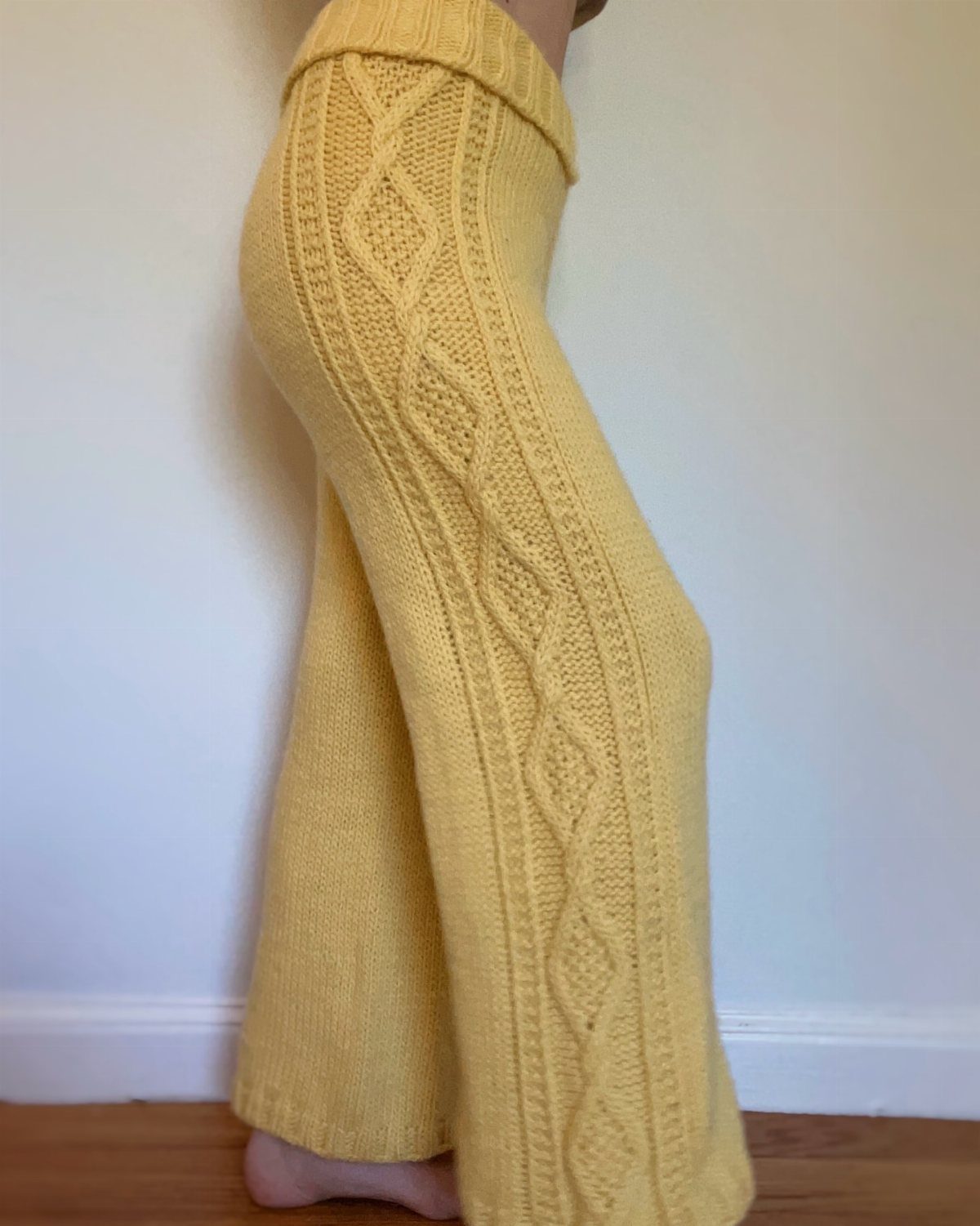 Person wearing yellow cable-knit chunky wide-leg pants against a white wall.