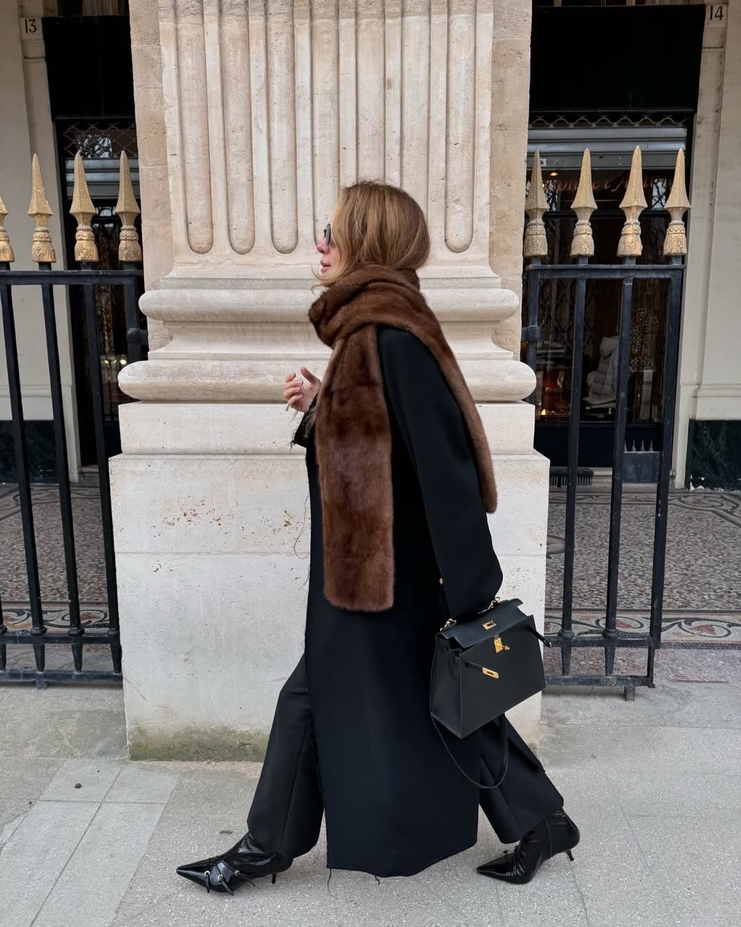 A woman walking in a black coat and a large brown faux-fur scarf.