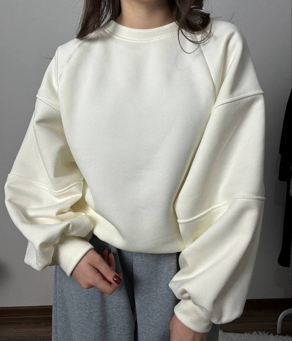A person wearing a cream oversized sweatshirt and grey sweatpants against a neutral background.