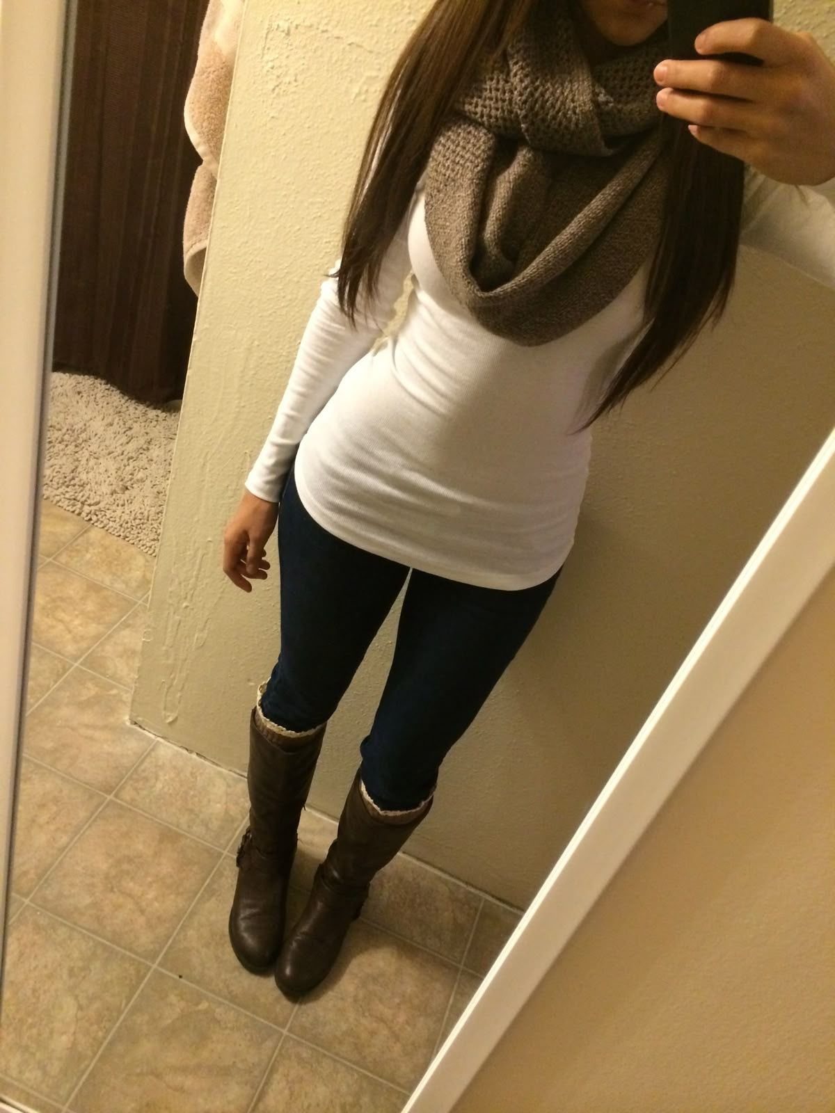 A person wearing dark wash skinny jeans, a white top, brown scarf, and brown boots.