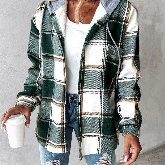 A person wearing a green plaid hooded shirt and distressed blue jeans while holding coffee.