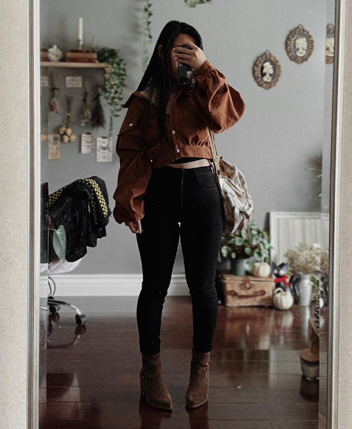 A woman posing in a mirror wearing a brown jacket and black jeans.