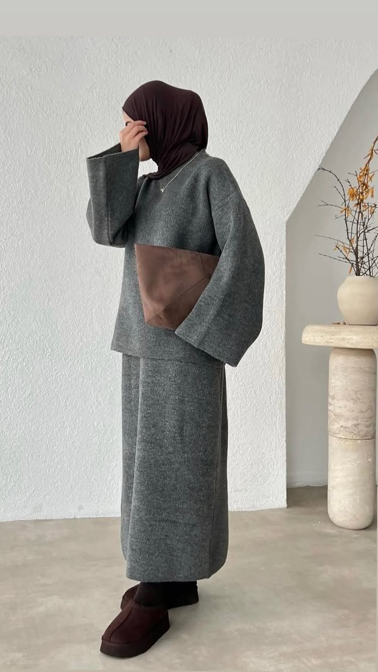A woman in a grey knit sweater and matching skirt with a brown hijab and clutch.