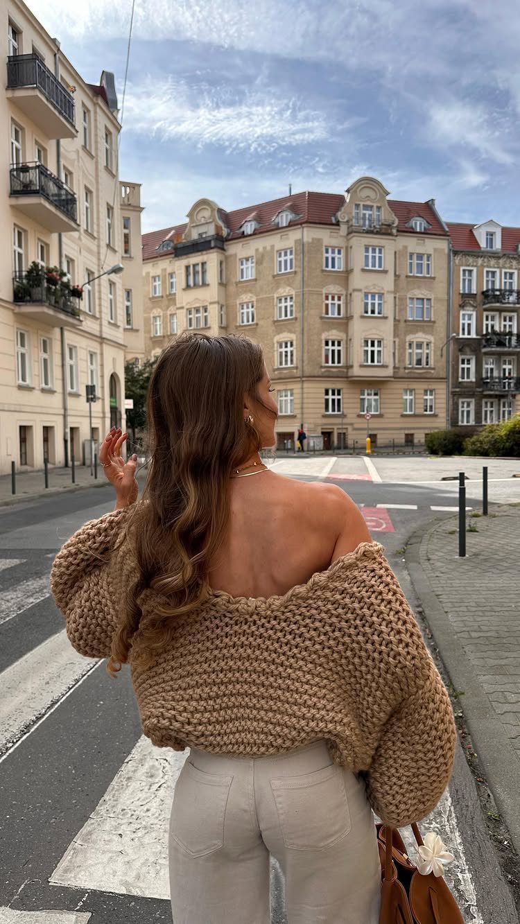 Woman wearing an oversized chunky knit tan sweater standing on a city street near a crosswalk.