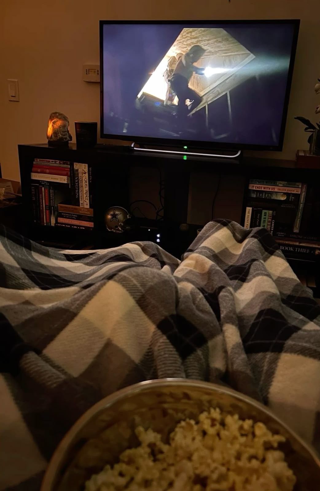 A television playing a movie with a plaid blanket and popcorn in the foreground.